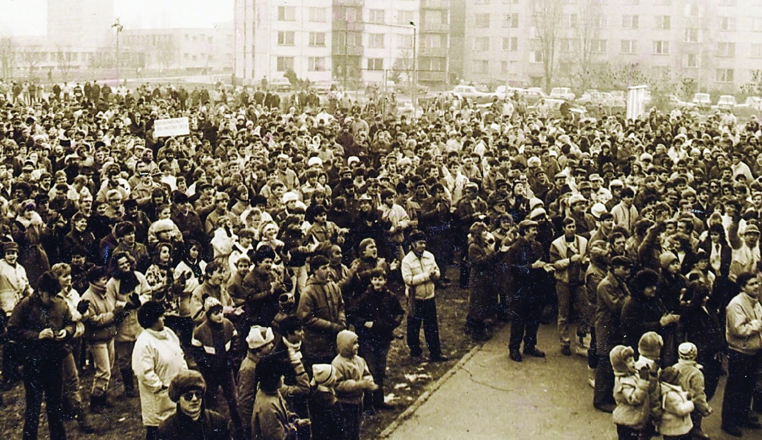 Dav ľudí na zhromaždení pri dome kultúry v Šali, v pozadí paneláky (červeno tónovaná fotografia)
