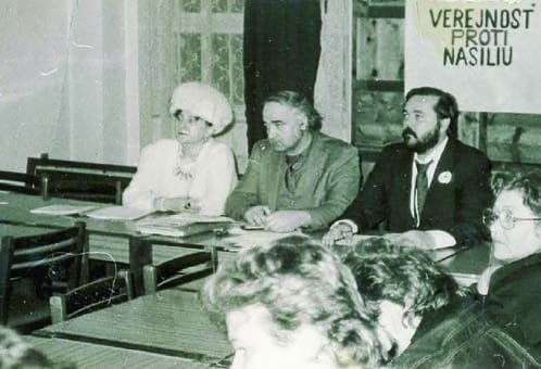 Mária Czelláriková, Jozef Kozaňák a Peter Nemes za stolom na stretnutí VPN, v pozadí plagát Verejnosť proti násiliu