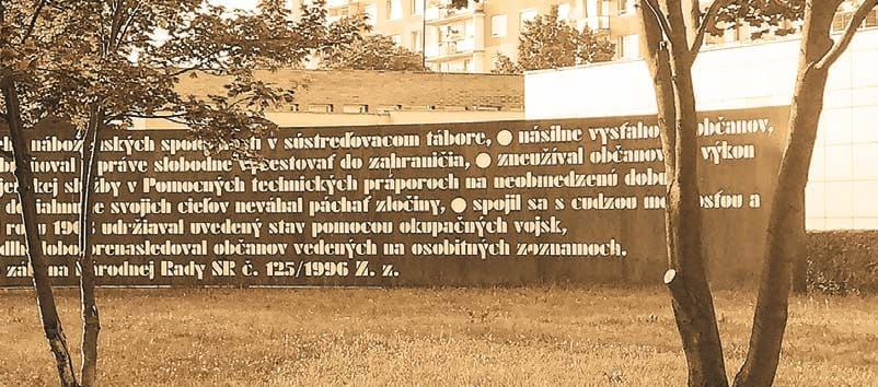 Detail Pamätníka 17. novembra – oceľová stena s vyrezaným textom zákona o nemorálnosti komunistického systému, pred ňou stromy